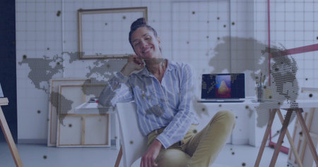 Smiling woman sitting on white chair in bright creative studio, with laptop and jar of paintbrushes. Artistic, innovative, contemporary, inspiring, professional, versatile, vibrantの写真素材