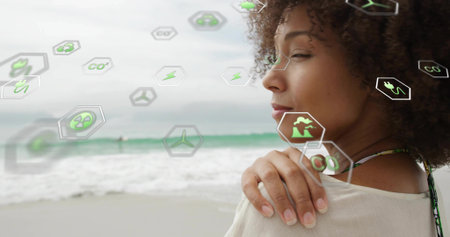 Standing woman in top facing right on beach, with floating eco icons, copy space. Sustainability, renewable, conservation, eco-friendly, climate, innovation, environmentalismの写真素材