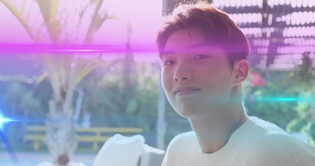 Sitting Korean boy wearing white knit sweater gazing off-camera at patio under pergola, copy space....