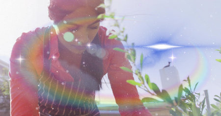 Asian gardener in striped apron leaning over leafy plants on balcony railing. Botanical, homegrown, nature, freshness, outdoor, serenity, organicの写真素材