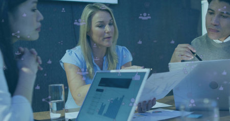 Colleagues reviewing graphs on laptops at meeting table, pointing at reports with social icons....