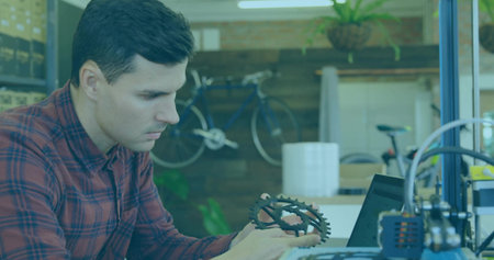 Inspecting engineer examining gear at makerspace bench, with laptop 3D printer bicycle plant boxes....