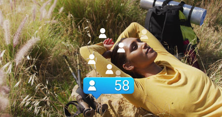 Reclining hiker in yellow top on rock in meadow, with backpack, hiking poles. Adventure, outdoor,...