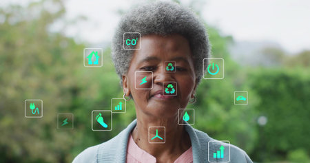 Standing senior woman wearing blue cardigan presenting floating eco and energy icons in garden. Sustainability, environmentalism, wellness, eco-friendly, empowerment, digital innovation, natureの写真素材
