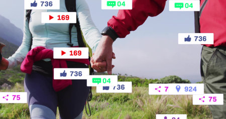 Walking mature hiking couple holding hands on grassy trail with packs poles smartwatch. Adventure, exploration, fitness, outdoors, nature, wellness, mountainsの写真素材