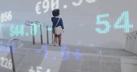 Mid adult woman descending concrete stairs at transit station, with currency data, copy space. Urban, transportation, financial, technology, data, modern, professionalの写真素材