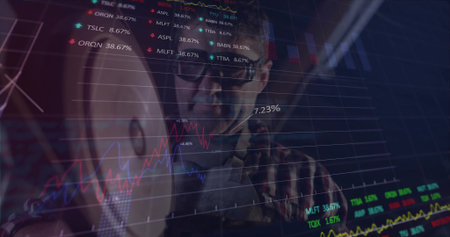 Analyzing trader in eyeglasses studying laptop in office, with colored line graphs and tickers....