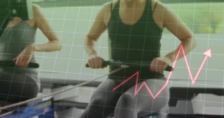 Rowing two athletic women pulling grips and pushing foot straps at gym studio, performance chart....