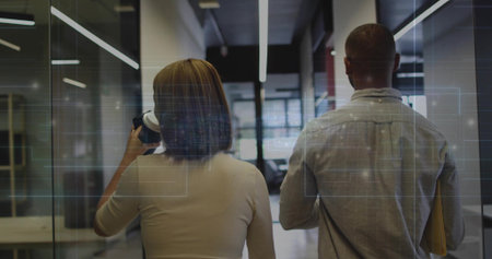 Walking office coworkers holding coffee cup, manila folder at glass corridor, with data overlays....