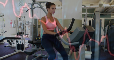 Pedaling woman wearing pink sportswear on exercise bike in gym, with heart-rate graph overlay....