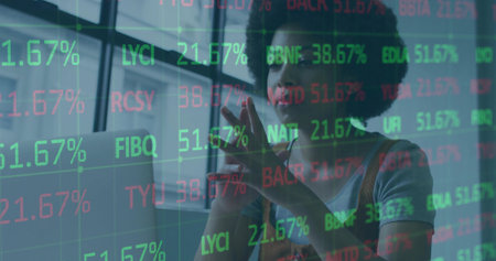 Standing analyst in overalls examining stock tickers on touchscreen in office with laptop. Finance,...