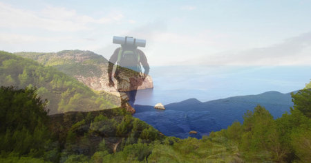 Standing male hiker surveying rocky outcrop overlooking blue bay, with green backpack, sleeping mat. Adventure, exploration, wilderness, landscape, trekking, outdoor, natureの写真素材