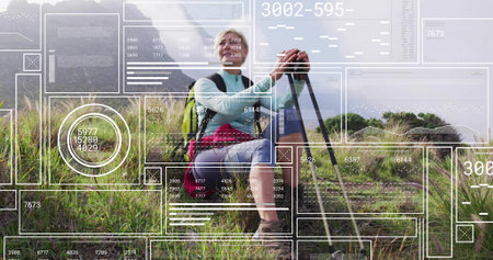 Pausing woman hiker in hiking boots holding trekking poles on grassy hillside, with green backpack. Adventure, exploration, endurance, outdoor, landscape, fitness, naturalの写真素材