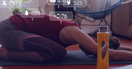 Holding woman in athletic wear in child's pose on yoga mat at home, with water bottle. Wellness, relaxation, fitness, home, mindfulness, simplicity, strengthの写真素材