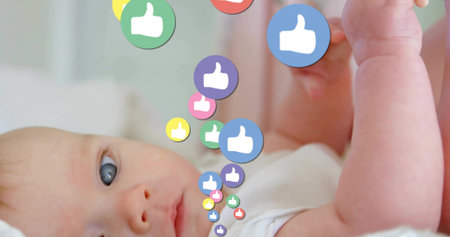 Infant wearing white onesie lying on bed in nursery, looking at colorful thumbs-up icons descending....