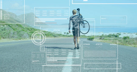 Walking mid-adult man carrying bicycle over shoulder on coastal highway road, with data overlays. Adventure, exploration, technology, outdoor activity, travel, fitness, scenicの写真素材
