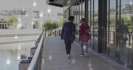 Two business casual colleagues walking waterfront walk with black shoulder bag and canal railing....