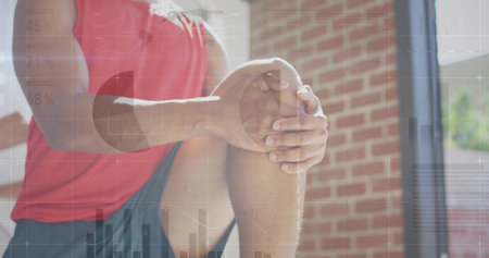 Grasping opposite knee while kneeling in gym area, wearing red sportswear with floating data charts. Fitness, analytics, health, performance, innovation, determination, modernの写真素材