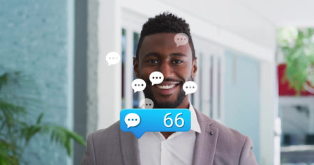 Businessman in gray suit smiling inside office lobby, with chat icons and notification 66. Professional, urban, corporate, modern, communication, collaboration, networkingの写真素材