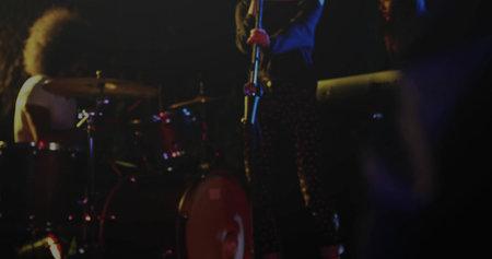 Singer in patterned pants performing on stage holding mic stand, with red drum kit and lights. Performance, concert, nightlife, stage, rhythm, entertainment, acousticの写真素材