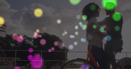 Leaning couple holding bicycle on waterfront by metal railing at sunset with bokeh, copy space. Romantic, outdoor, vibrant, scenic, leisure, connection, atmosphericの写真素材