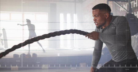 Swinging battle rope man building strength in gym by windows with grid overlay, copy space. Fitness, training, strength, athleticism, industrial, workout, cardioの写真素材