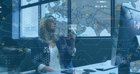 Analyst wearing blazer manipulating world map overlay at office desk, using stylus and smartphone....