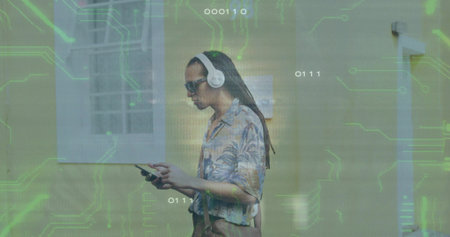 Walking man on street past wall wearing floral shirt, headphones, carrying bag under circuitry....