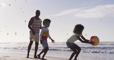 Playing father with children tossing beach ball on wet sand at ocean shoreline, with star confetti. Family, outdoor, playful, vibrant, leisure, celebration, joyfulの写真素材