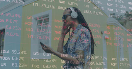 Man wearing tropical shirt sunglasses and headphones viewing market data on phone by pastel homes. Casual, urban, vibrant, modern, lifestyle, technology, leisureの写真素材