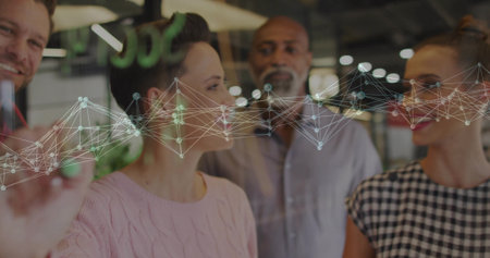 Four colleagues standing behind glass board discussing network graph in office, with green marker....