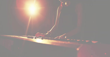 Female musician wearing sleeveless top playing electric keyboard on dark stage, with spotlight....