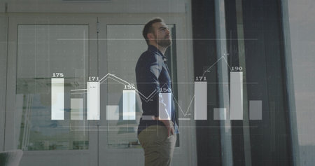 Standing man in modern office reviewing bar and line chart overlays on glass doors with blinds. Corporate, analytics, productivity, professional, sleek, datasets, businessの写真素材
