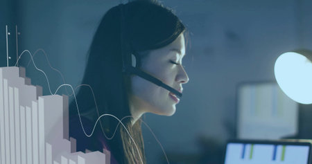 Analyzing charts adult Chinese woman wearing headset at office desk, with glowing monitor overlay....