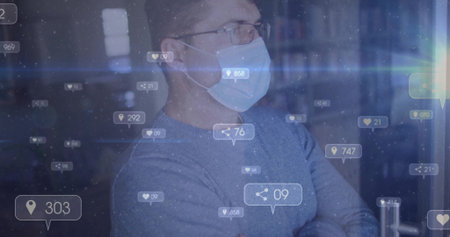 Standing man wearing glasses and mask behind glass panel at library, with digital overlay icons....