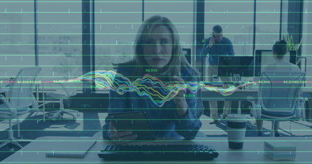 Analyzing charts, female professional holding tablet at open-plan office, with keyboard, coffee cup. Corporate, productivity, modern, technology, teamwork, collaboration, sleekの写真素材