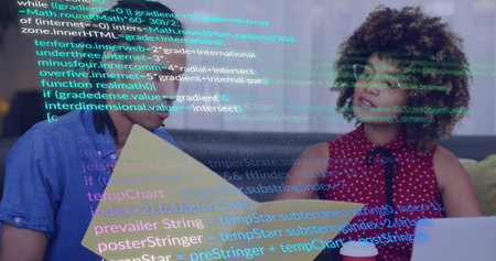 Coworkers reviewing code overlay on office grey sofa, holding yellow folder laptop red coffee cup. Collaboration, teamwork, technology, innovation, modern, casual, workspaceの写真素材