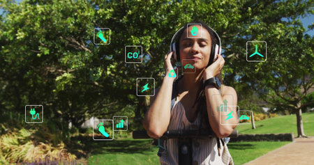 Listening woman with over-ear headphones and smartwatch holding scooter on park path with eco icons....