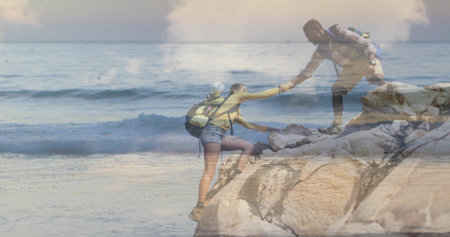 Two people helping each other climb rocks by the oceanの写真素材