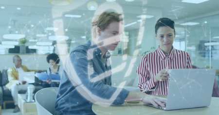 Collaborating two colleagues reviewing report on laptop at table in open office, with coffee mug. Modern, productive, teamwork, casual, creative, professional, contemporaryの写真素材