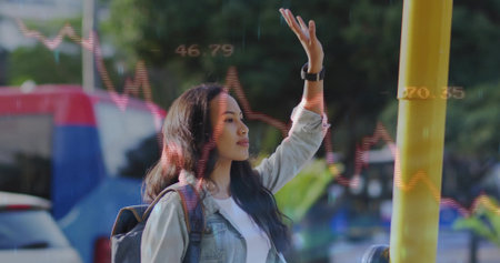Raising hand female commuter signalling bus at stop pole with backpack smartwatch. Urban, transportation, technology, casual, modern, outdoorの写真素材