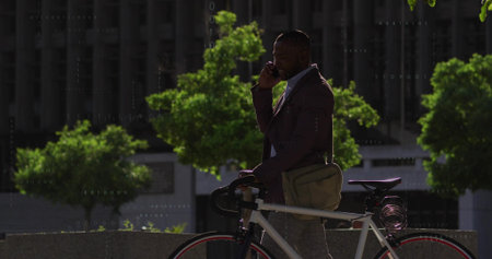 Talking businessman in blazer holding smartphone and white bike on city terrace, with messenger bag. Urban, professional, lifestyle, vibrant, communication, outdoors, modernの写真素材
