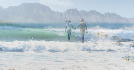Walking couple wearing light blue and light green shirts wading in water at beach, with rocks. Romantic, connection, tranquility, scenery, adventure, leisure, harmonyの写真素材