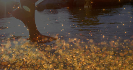 Wading legs and feet in shorts through shallow water at sunset, with golden bokeh reflections....