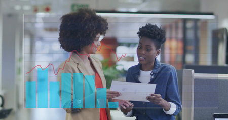 Two coworkers wearing business attire reviewing report in open plan office with chart overlay. Collaboration, analytics, business, teamwork, professional, technology, workspaceの写真素材