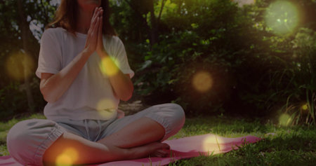 Sitting woman wearing workout clothes holding prayer pose on pink yoga mat in backyard, copy space....