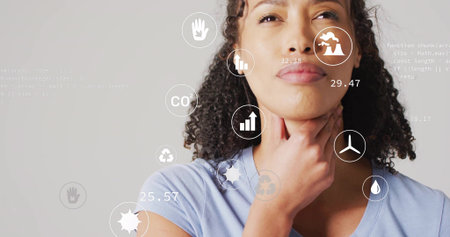 Touching neck woman wearing blue tee analyzing environmental icons and code in studio, copy space. Sustainability, data visualization, environmental monitoring, technology, eco-conscious, analytical, modern designの写真素材