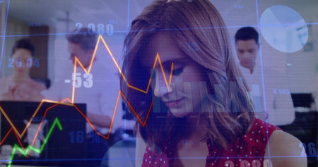 Woman in red polka dot blouse analyzing financial data in open office, with laptops, chart overlays....