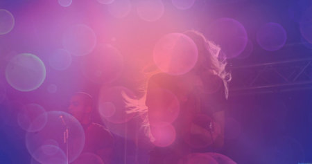 Performing female musician singing into microphone on stage, with purple-pink lighting and trusses....