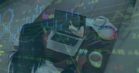 Watching student holding smartphone at home desk, with laptop, supplies, coffee mug, stock charts. Educational, e-learning, modern, workspace, digital, professional, innovativeの写真素材